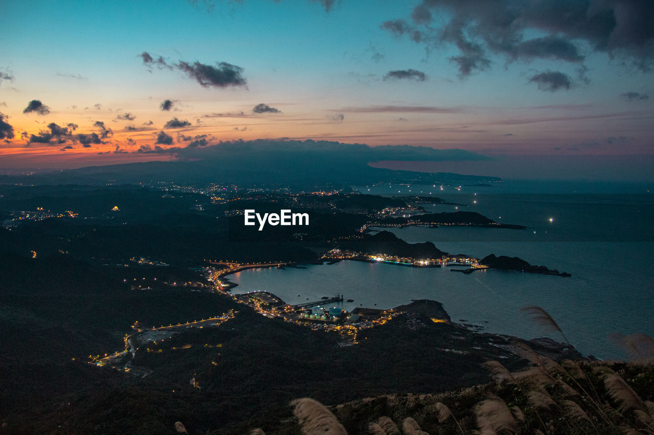 High angle view of sea and cityscape against sky during sunset