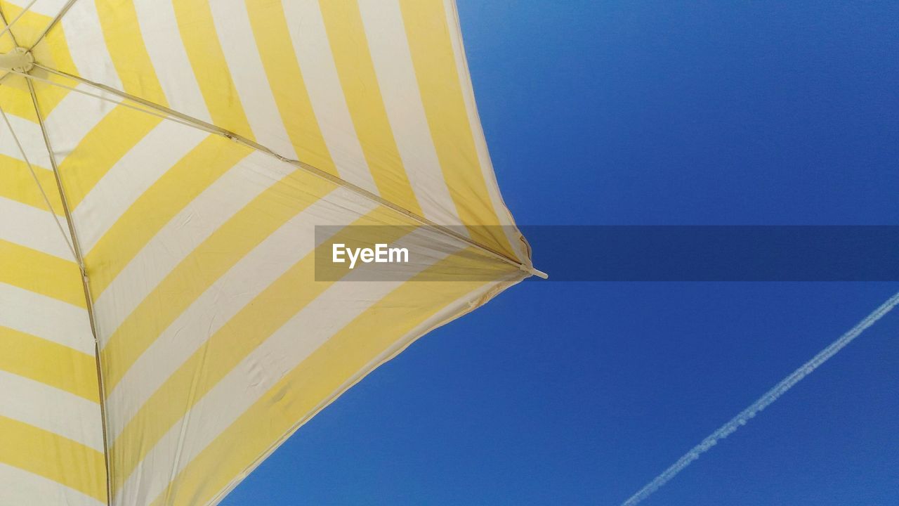 Cropped image of striped beach umbrella against blue sky with vapor trail