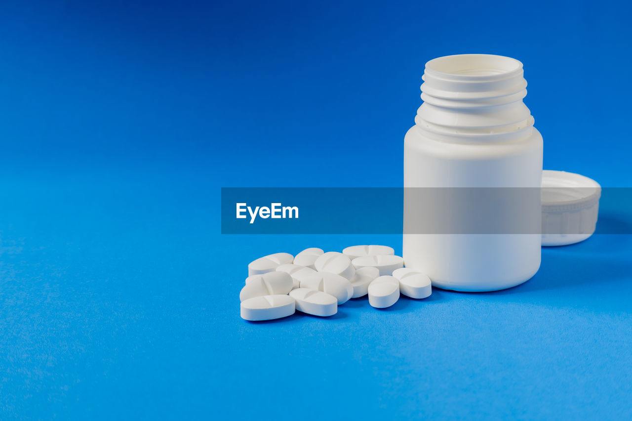 close-up of capsules spilling from bottle against blue background