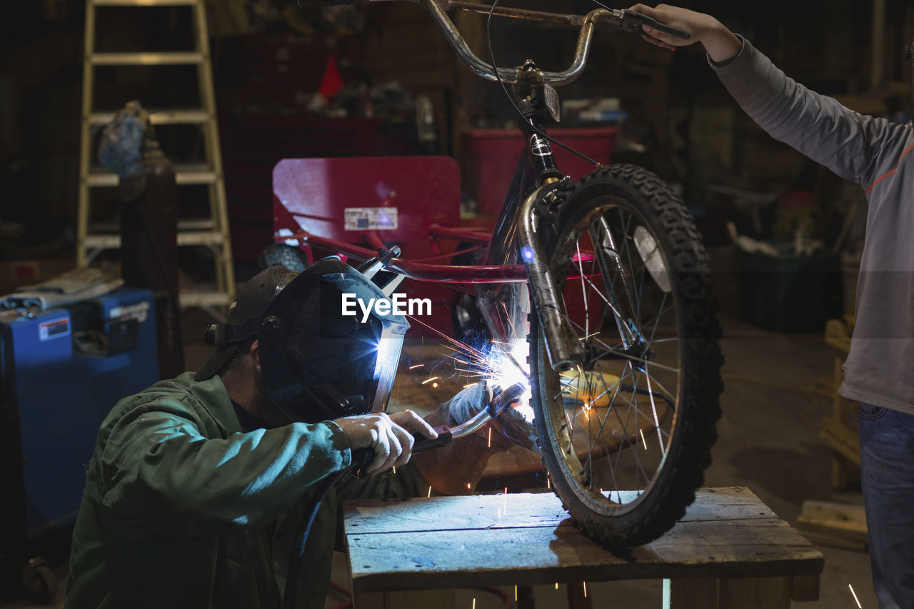 Father and son welding tricycle while working in workshop