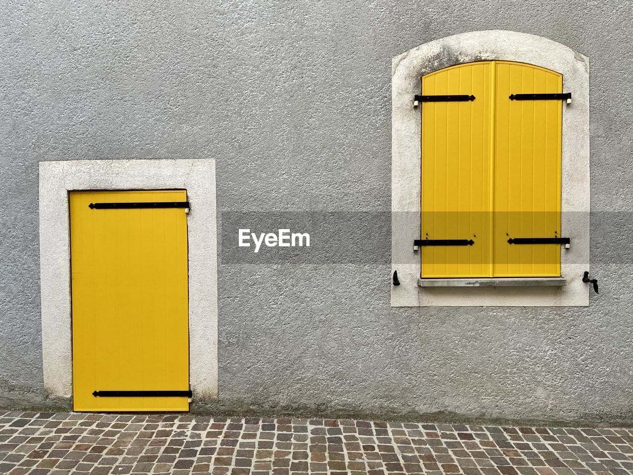 Closed yellow door and wooden shutters on the facade of the grey house 