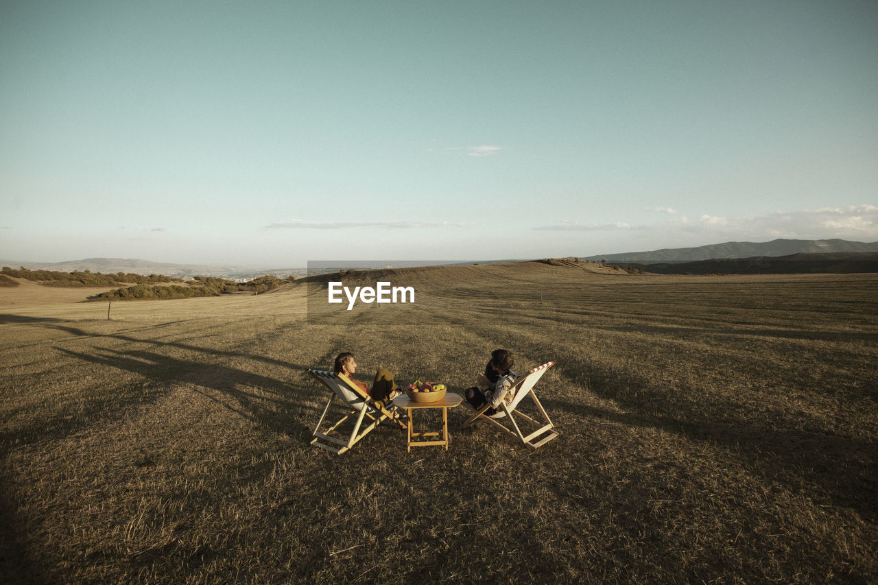 High angle view of friends sitting chairs at field against sky