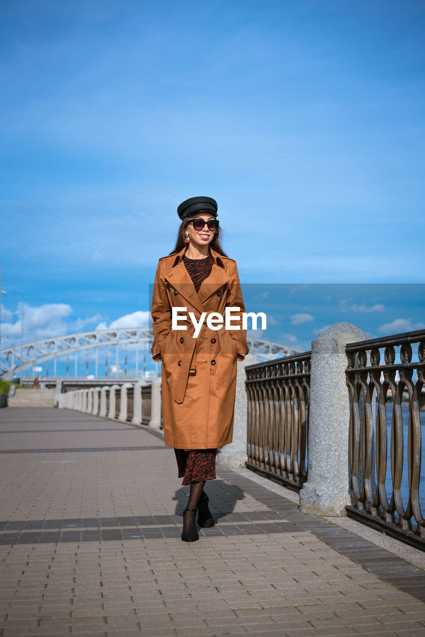 Beautiful woman in a cap and jacket posing while standing on the embankment