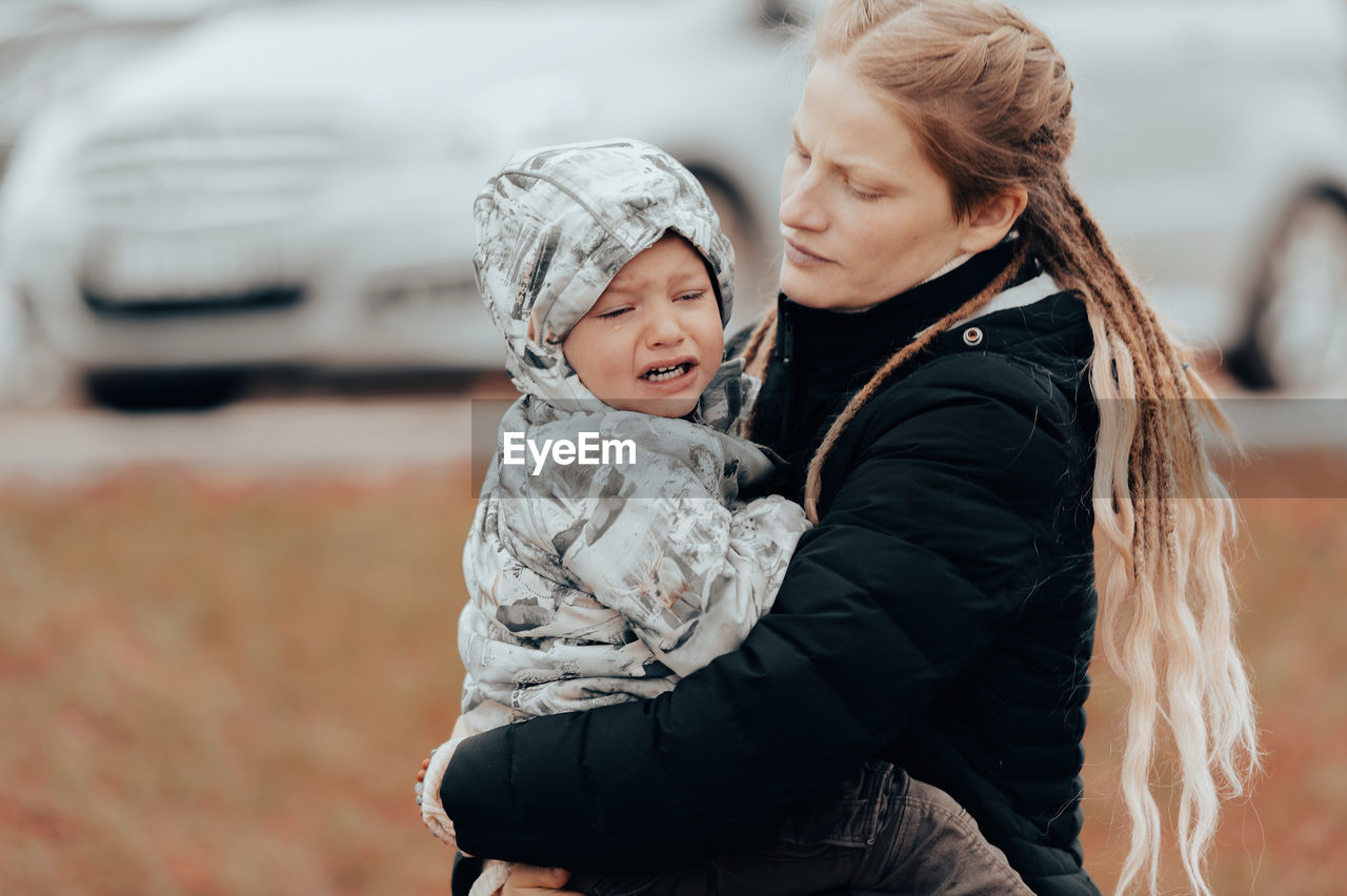 Mother holding crying baby, sad little boy being hugged by his mother