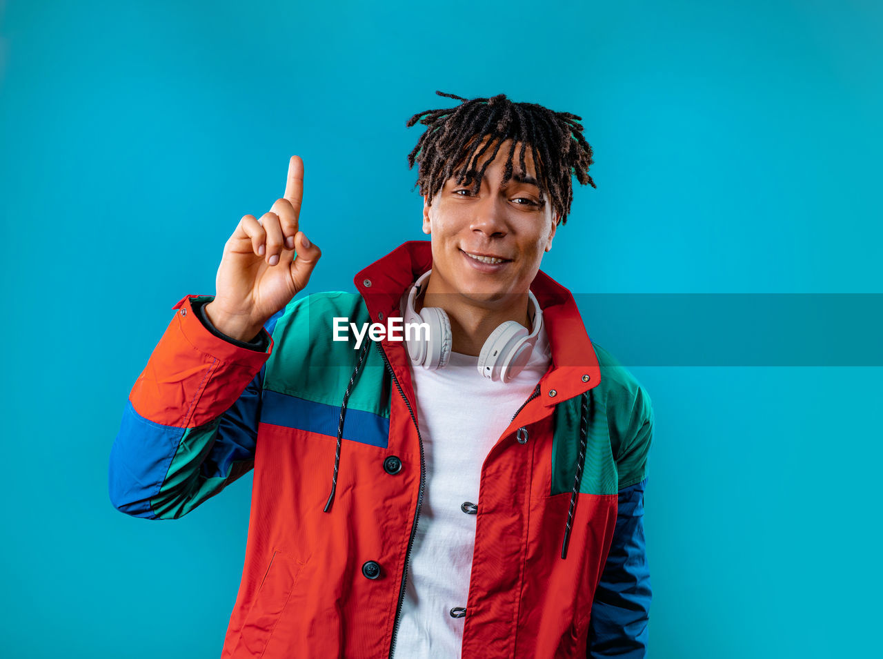 one person, colored background, studio shot, portrait, clothing, smiling, emotion, adult, happiness, person, blue, waist up, men, looking at camera, blue background, young adult, front view, indoors, gesturing, standing, jacket, fun, human face, red, positive emotion, copy space, cheerful, hand