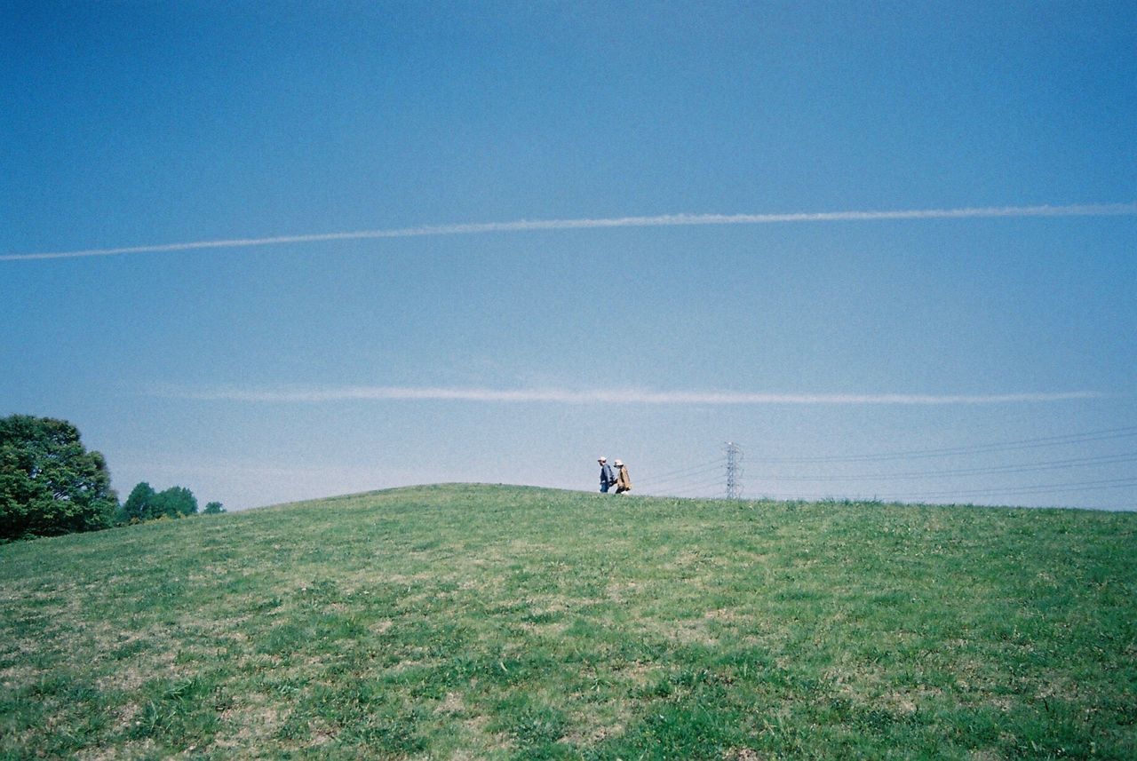 Man and woman walking on green field against blue sky