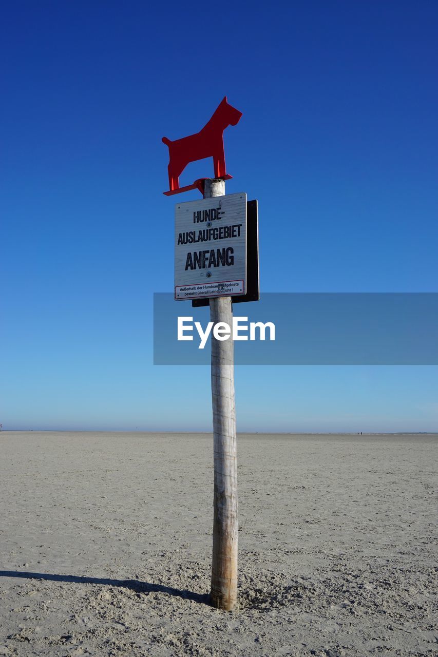 Information sign on beach against clear blue sky