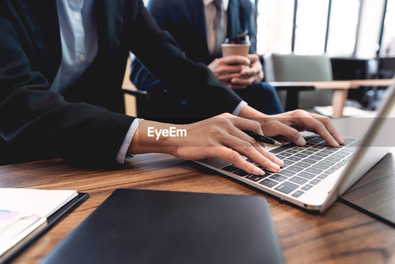 Midsection of colleagues discussing over laptop on desk in office