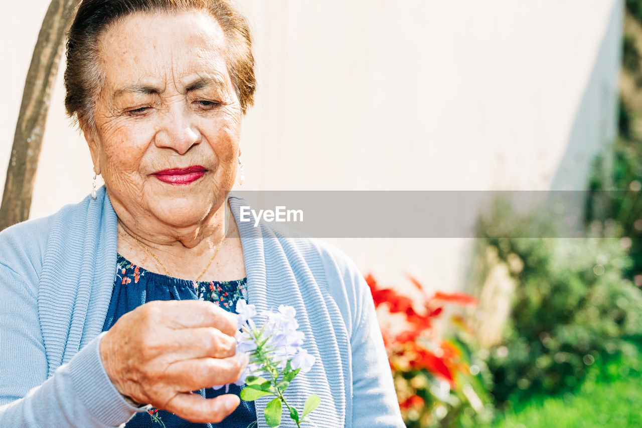 Senior woman holding a flower outdoors during the afternoon with copy space.