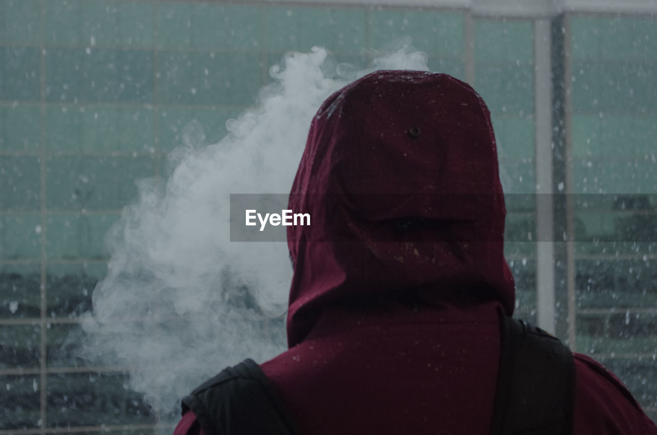 Rear view of person wearing hooded shirt with smoke during winter