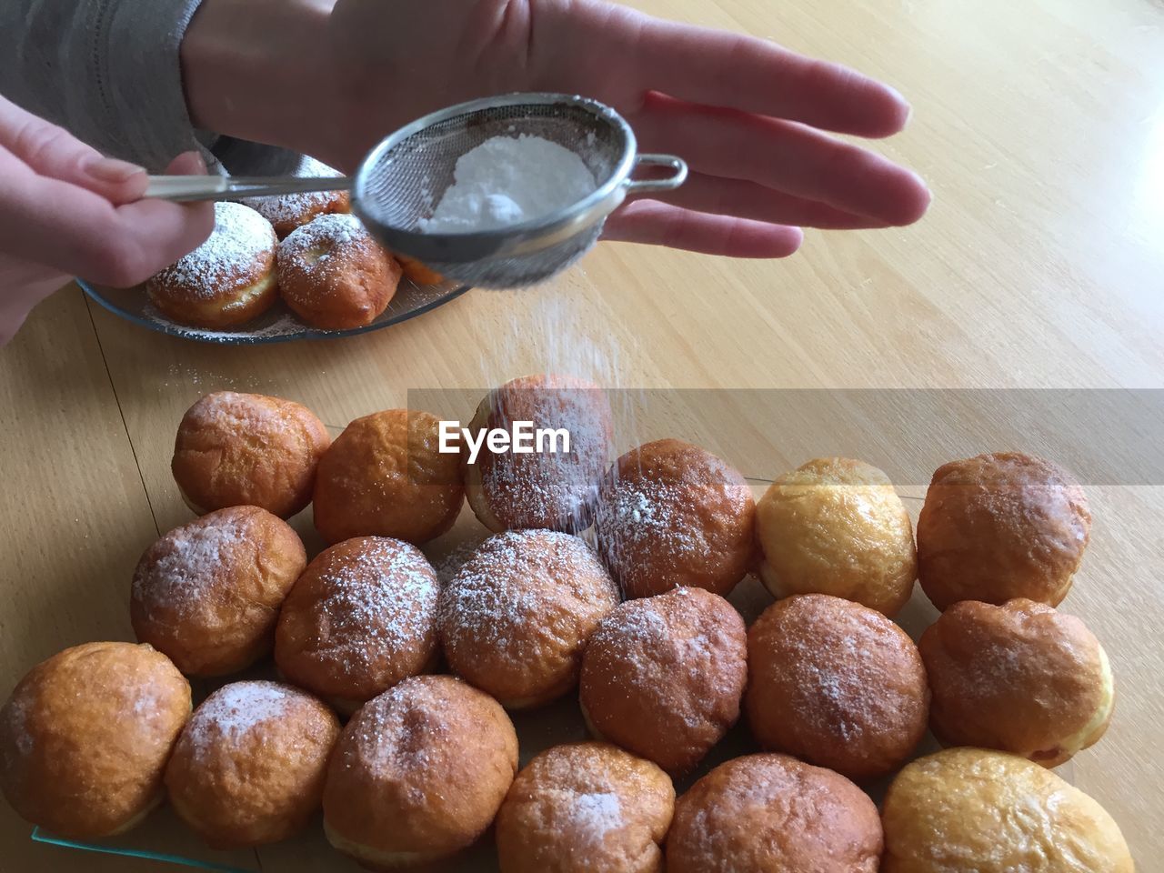 Cropped image of hand dusting powdered sugar on donuts