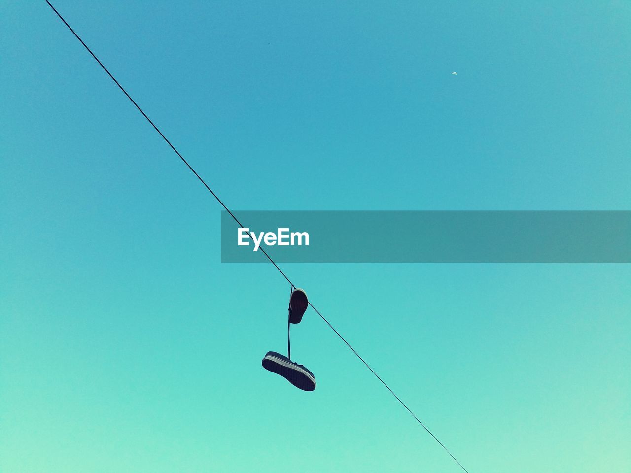 Low angle view of abandoned shoes hanging from cable against clear sky