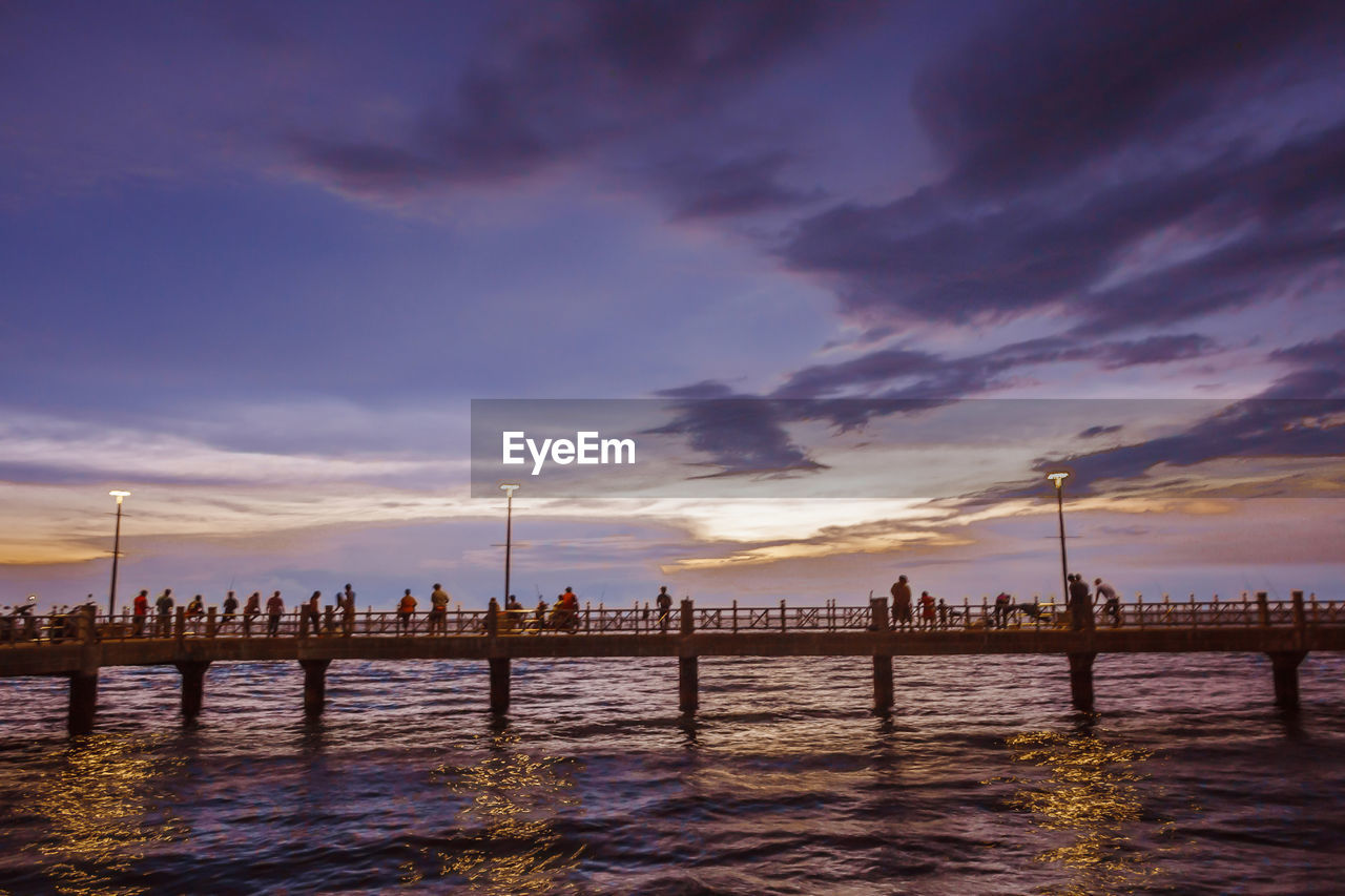 People on pier in sea against sky