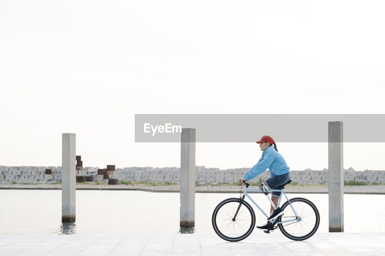 Young man riding bicycle on footpath against clear sky