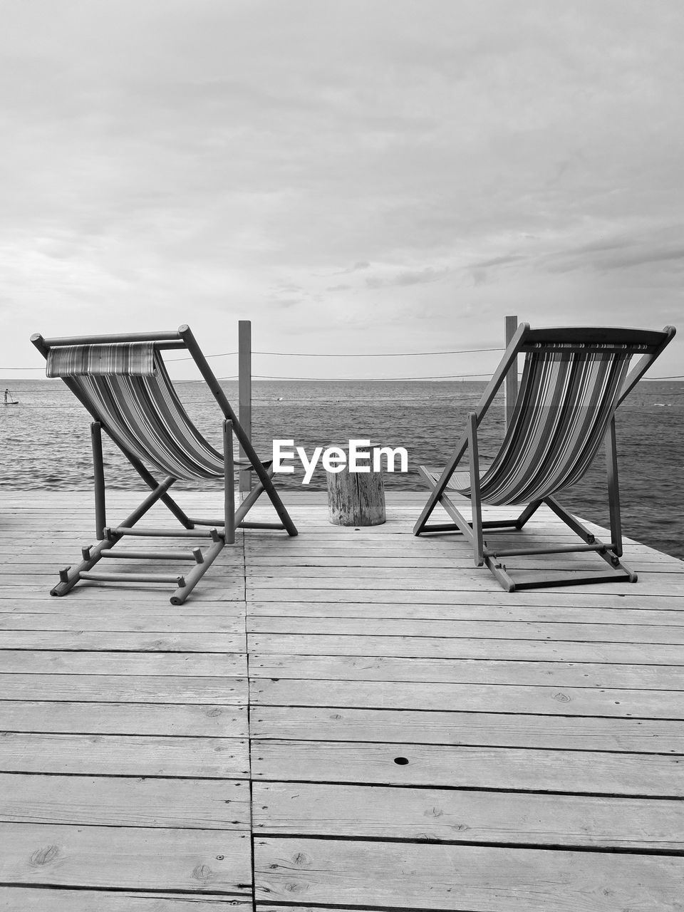 black and white, wood, water, sky, beach, land, sea, nature, monochrome photography, chair, seat, tranquility, absence, white, monochrome, tranquil scene, no people, horizon, horizon over water, day, scenics - nature, beauty in nature, sand, relaxation, empty, cloud, sitting, outdoors, deck chair, boardwalk, pier, summer, holiday, sunlight, trip, vacation, non-urban scene, idyllic