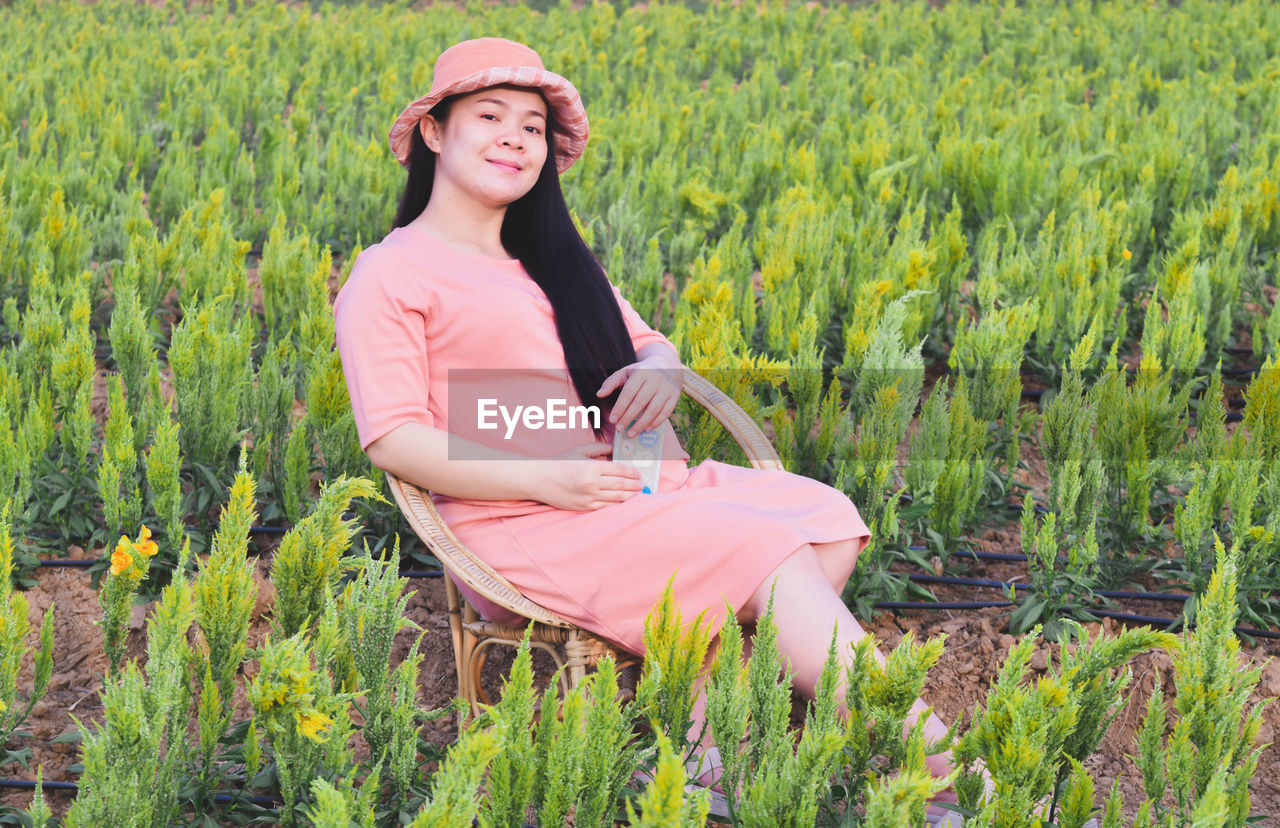 one person, plant, adult, meadow, women, field, nature, smiling, growth, landscape, land, rural scene, young adult, green, crop, agriculture, tranquility, portrait, happiness, beauty in nature, clothing, natural environment, leisure activity, hat, environment, three quarter length, lifestyles, day, female, flower, looking at camera, emotion, sitting, casual clothing, relaxation, outdoors, grass, farm, tranquil scene, hairstyle, long hair, occupation, summer, full length, grassland, side view, paddy field