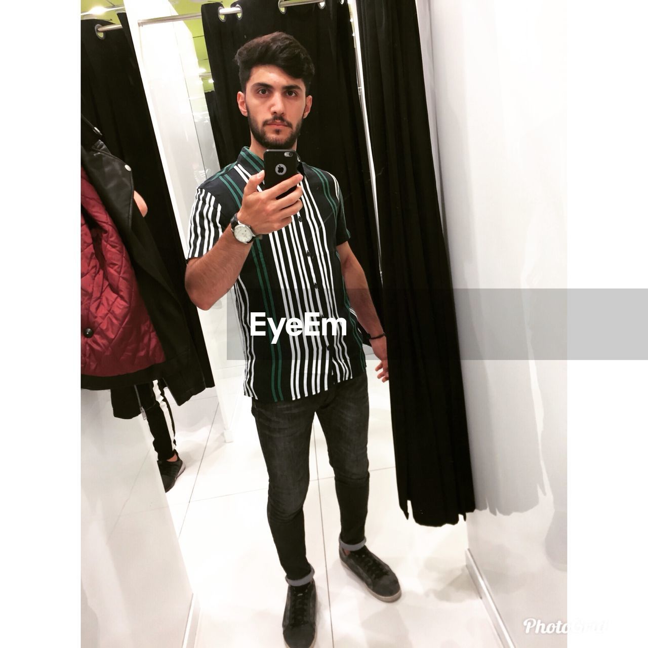 FULL LENGTH OF YOUNG MAN USING PHONE WHILE STANDING IN MIRROR