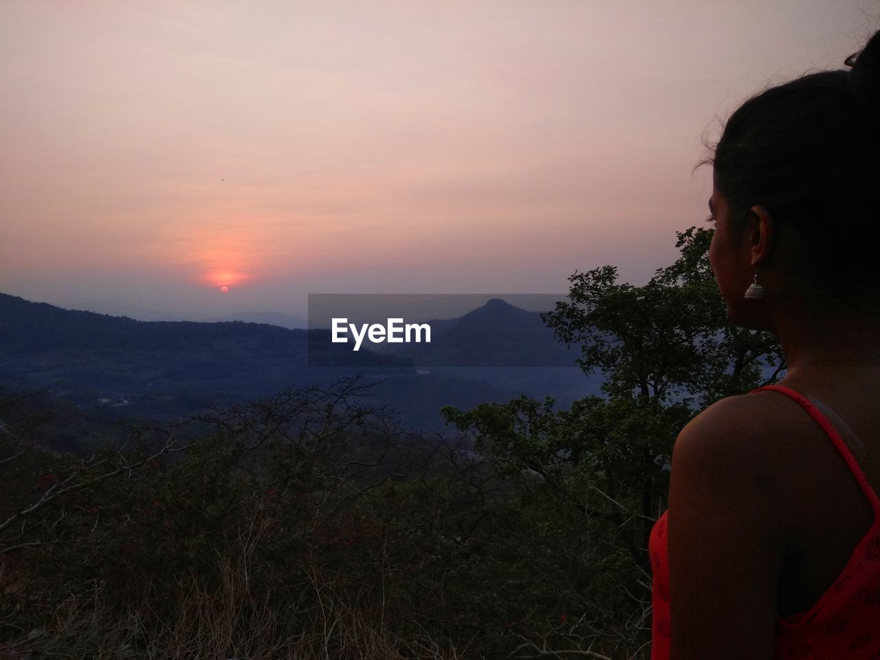 Side view of woman looking at mountains against sky during sunset