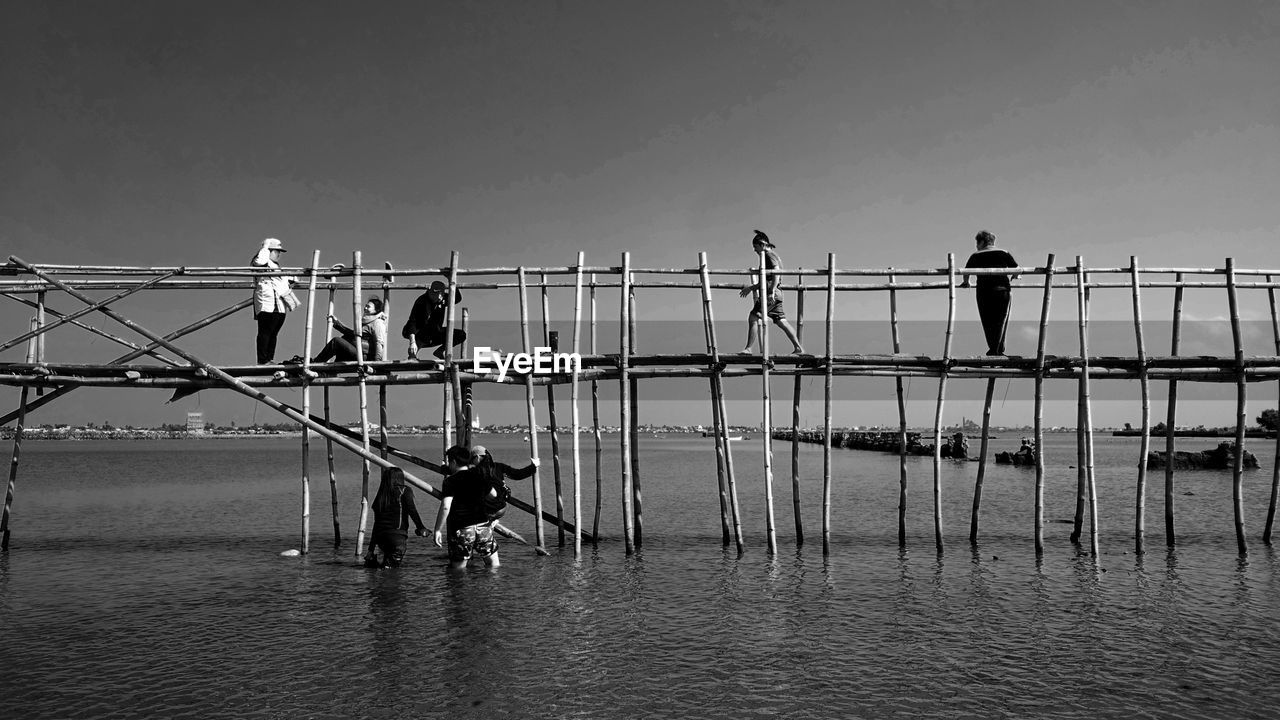 PEOPLE STANDING BY RAILING AGAINST SEA