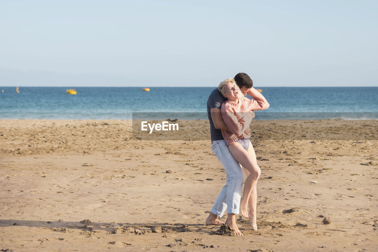 Cheerful couple embracing at beach against sky