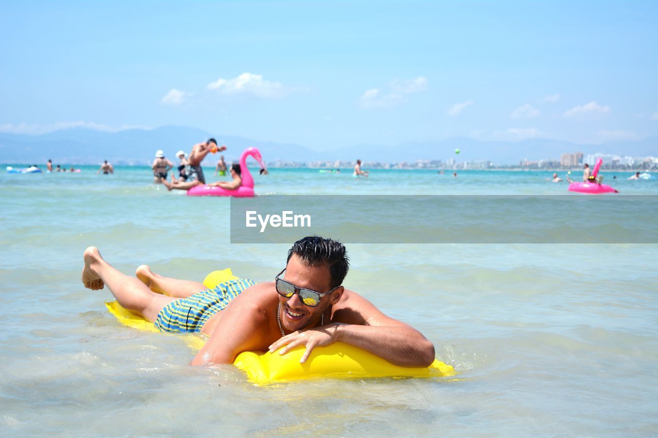 Shirtless young man relaxing on pool raft in sea against sky
