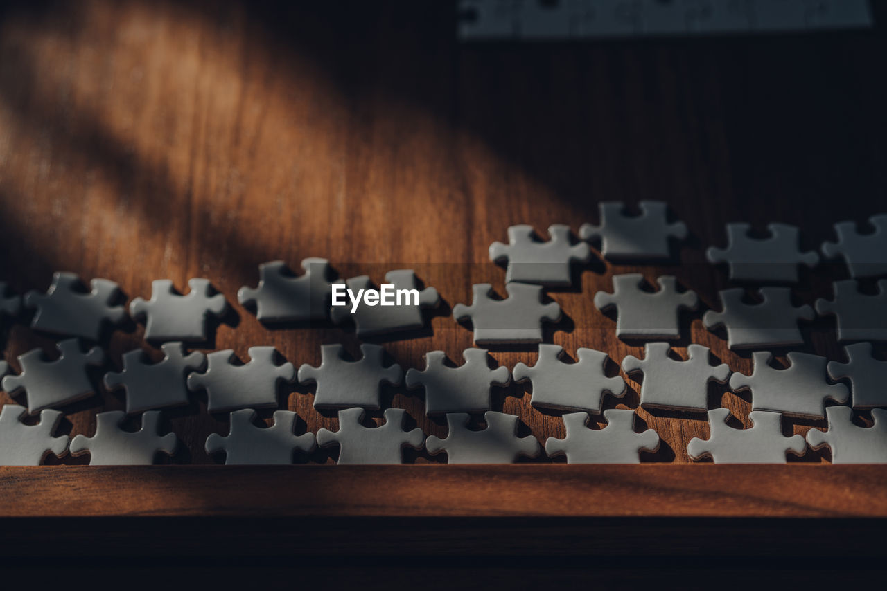 Sunlight from the window falls on white puzzle pieces on a wooden table, selective focus.