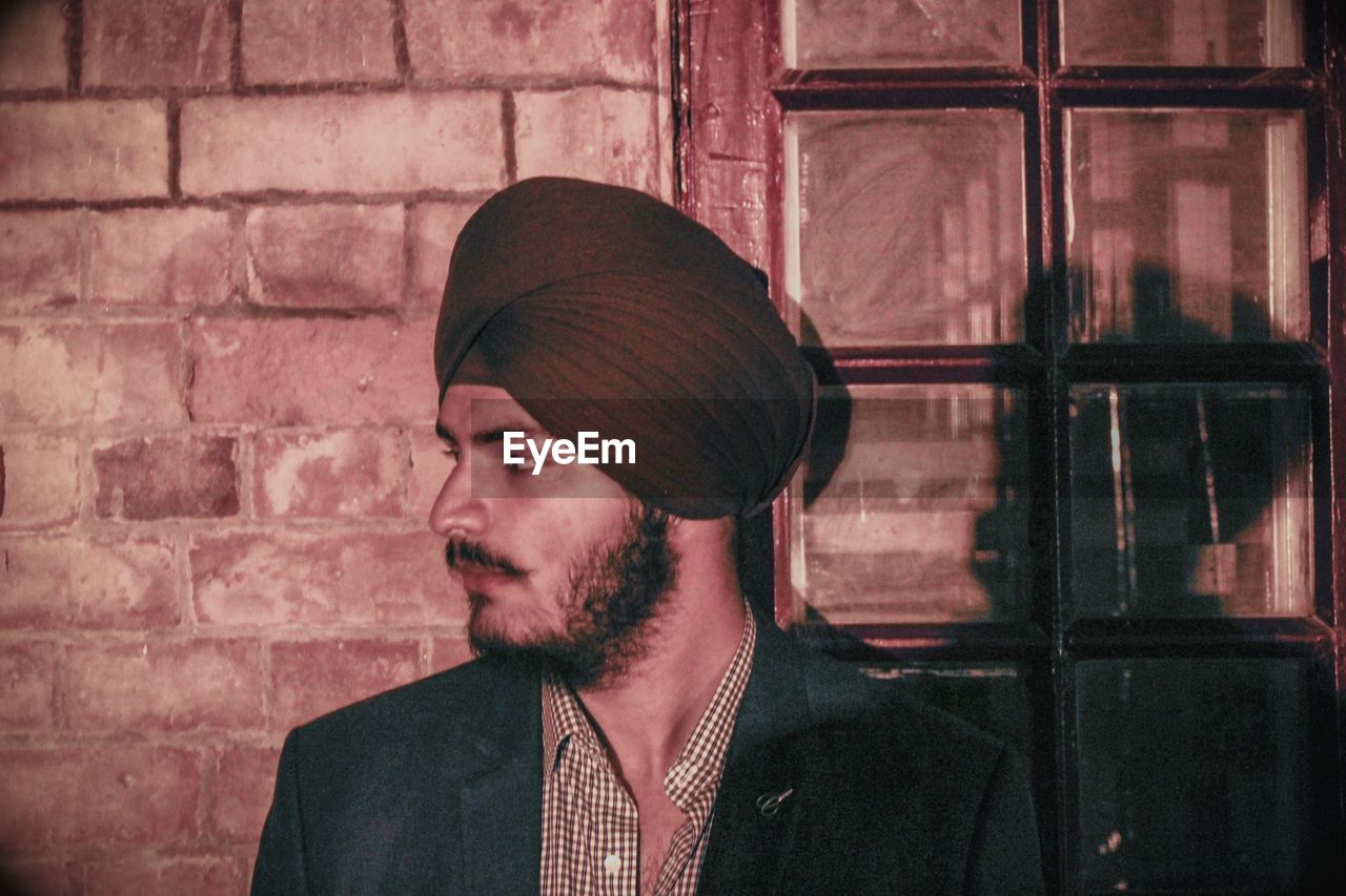 Thoughtful man wearing turban while standing against brick wall