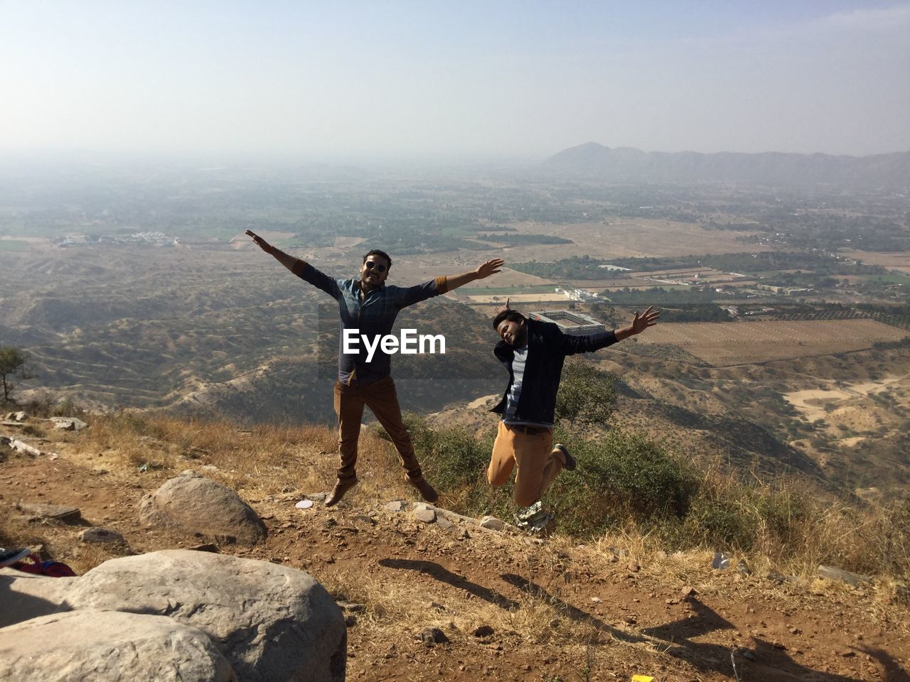 Full length of young men jumping on mountain against landscape