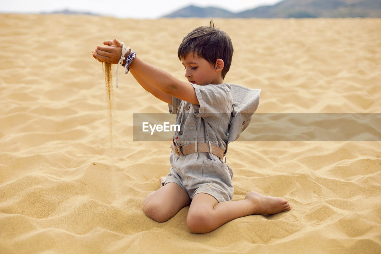 Portrait boy child traveler in a suit of an archaeologist and wearing hat sitting on sand in desert