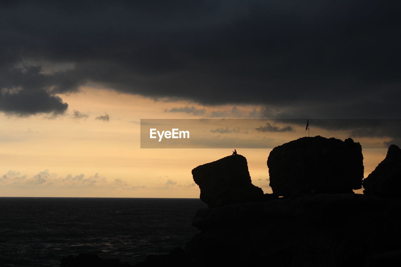 Silhouette rocks on shore against sky during sunset