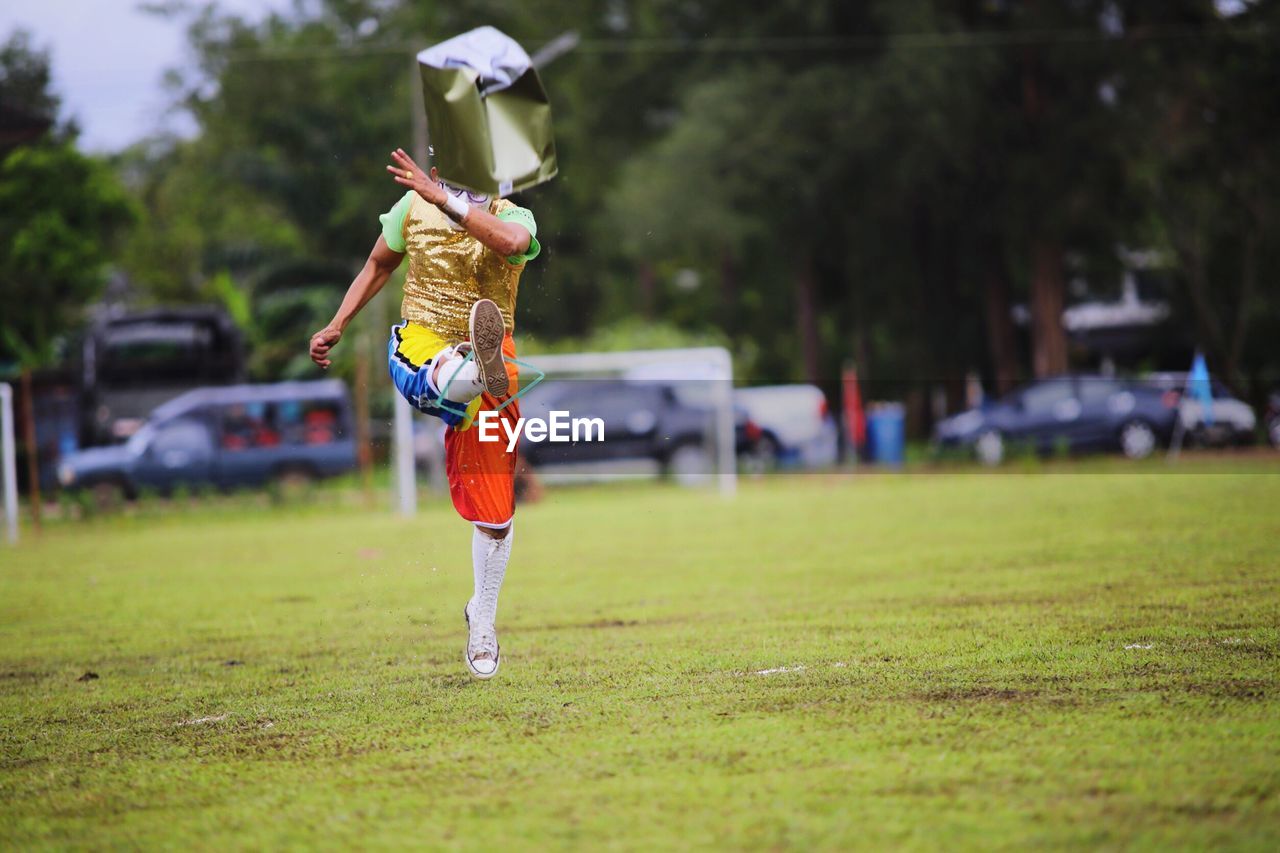 Man kicking container while standing on grassy field