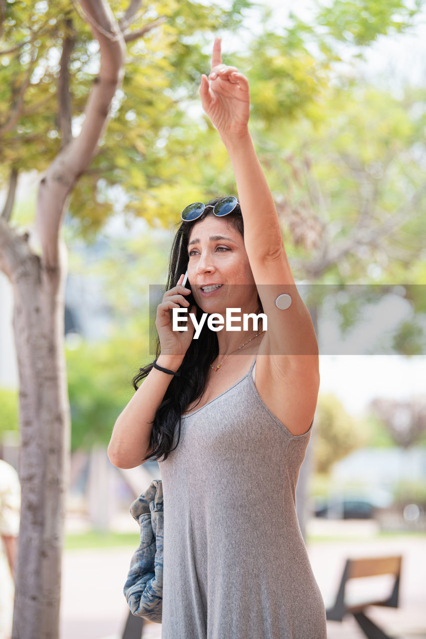 Adult woman with a glucose sensor device on her left arm talking with phone and calling a taxi