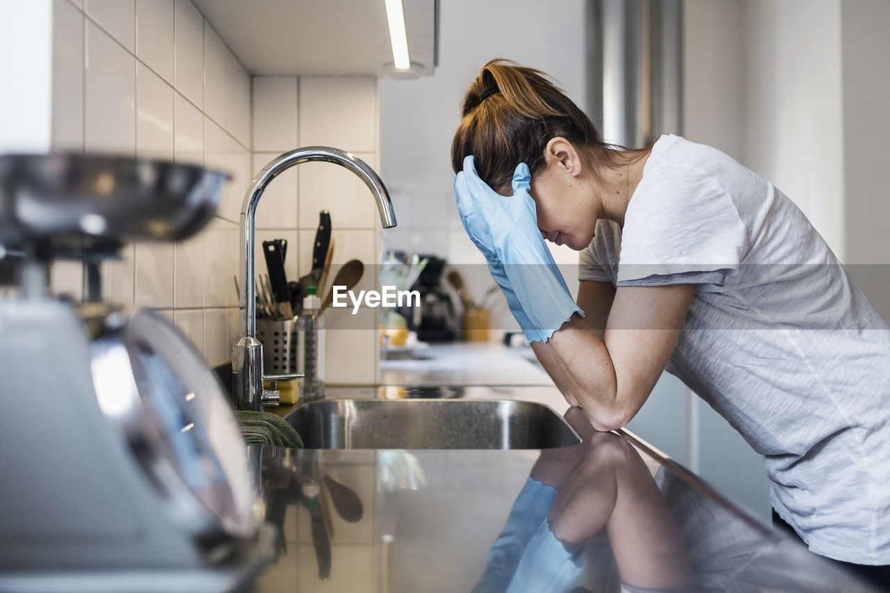 Side view of tensed woman leaning at sink in kitchen