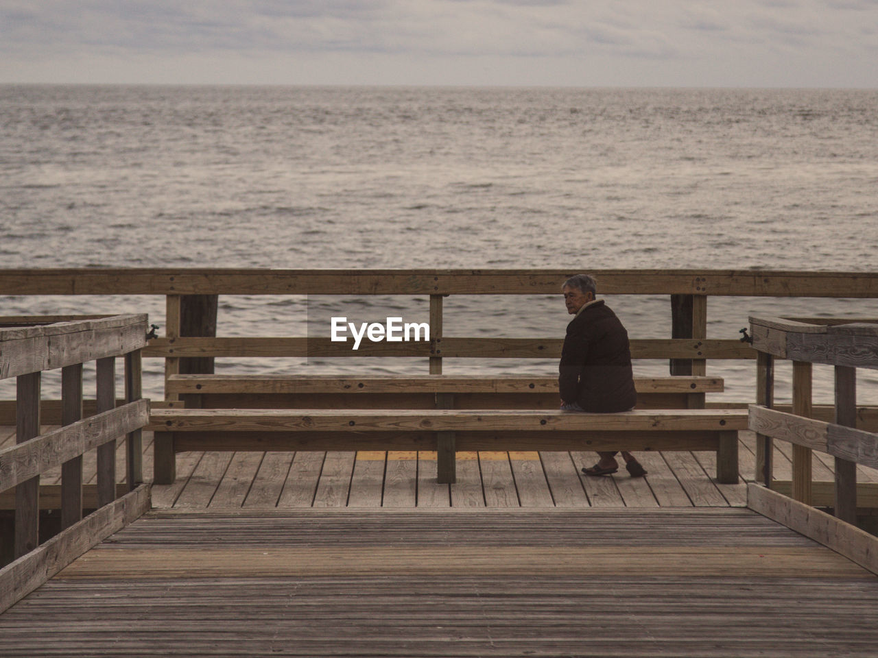 Rear view of man sitting on bench by sea