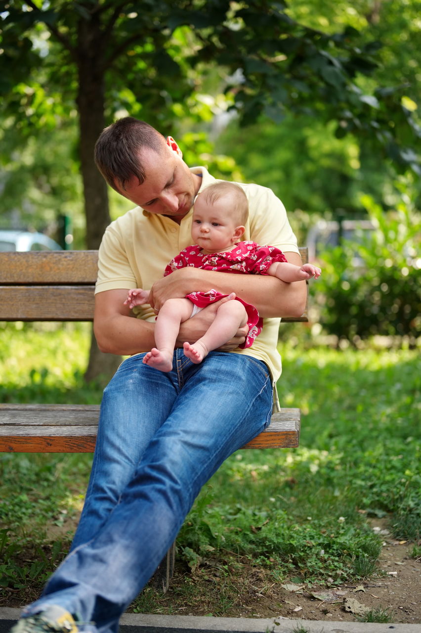 Father sitting on a bench in the park and holding his little baby girl