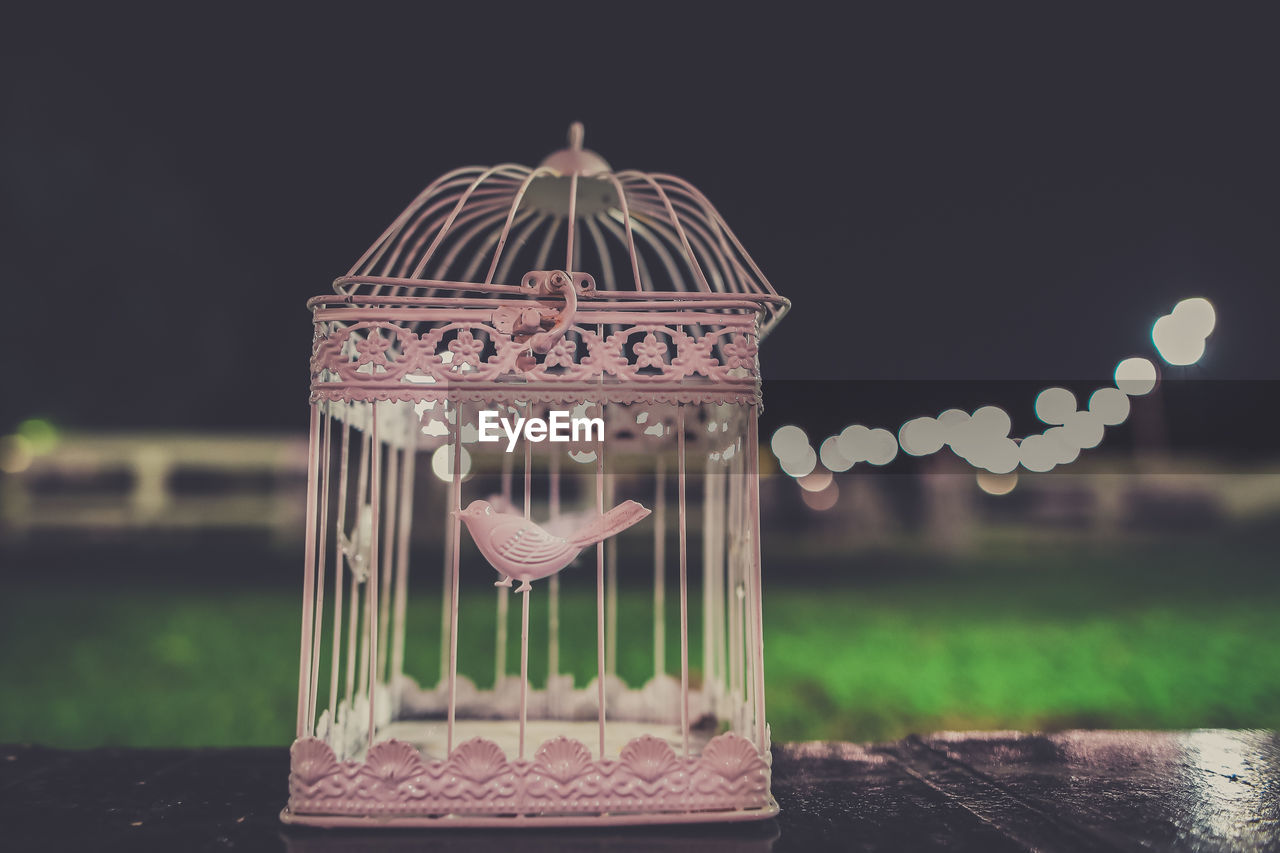 Close-up of empty birdcage on wooden table against sky at night