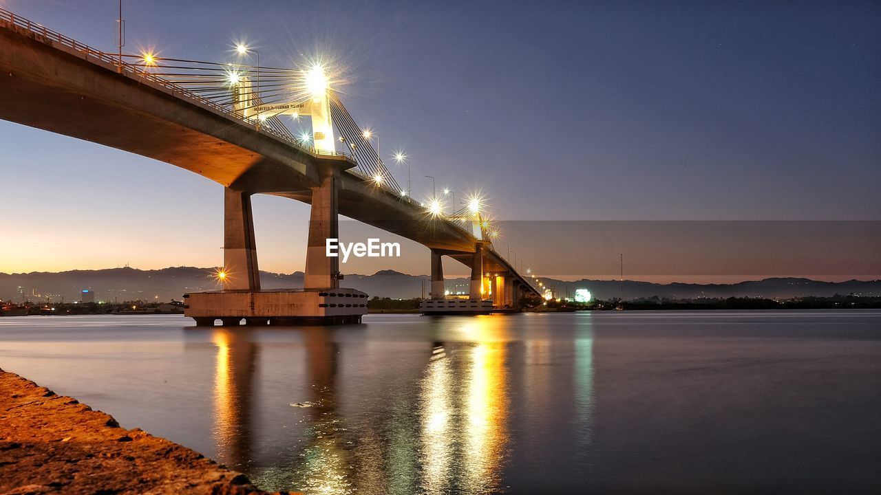 Illuminated marcelo fernan bridge over sea against sky at dusk
