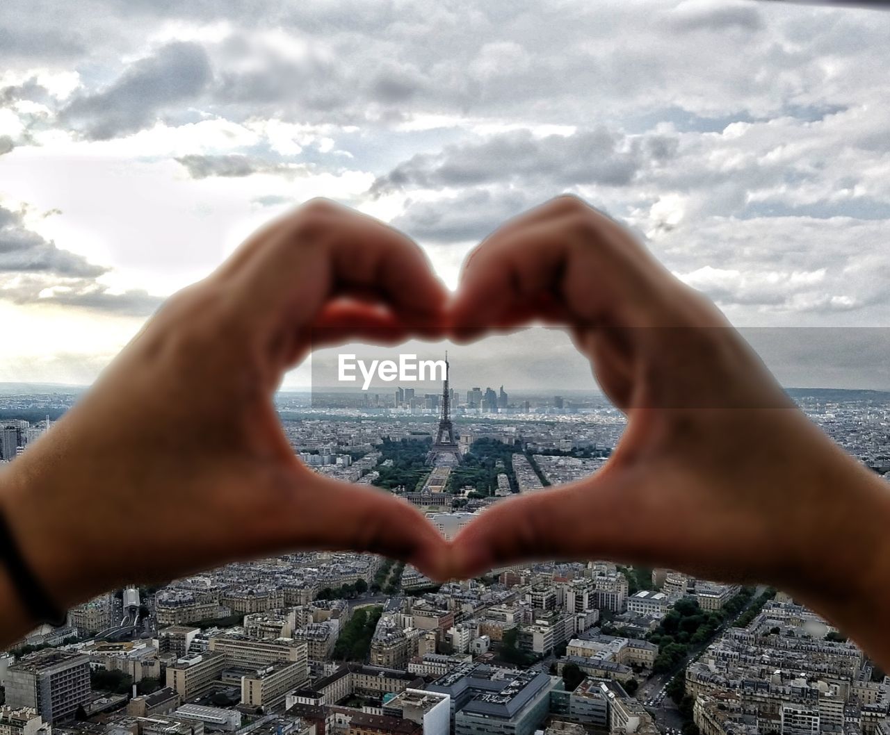 Close-up of hands making heart shape against eiffel tower