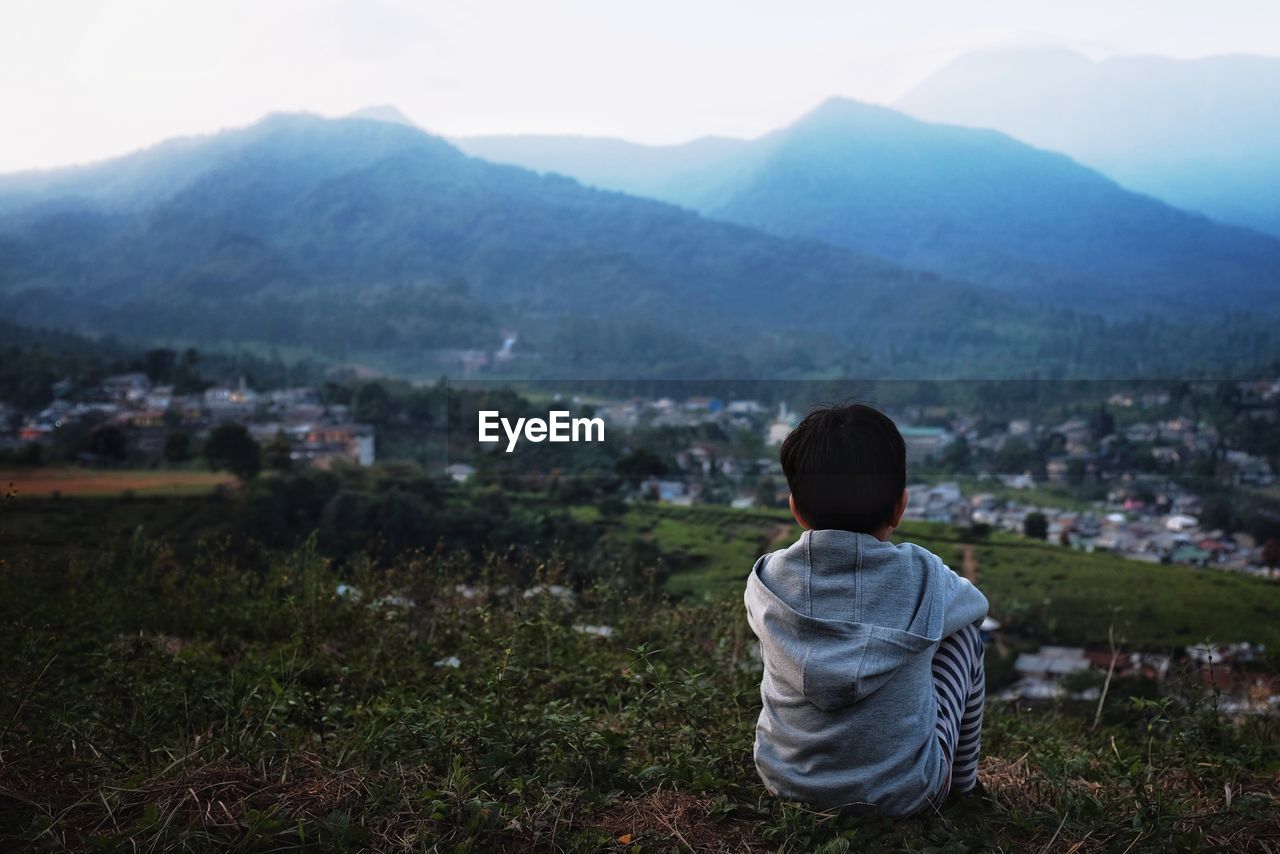 Rear view of boy sitting on mountain against sky