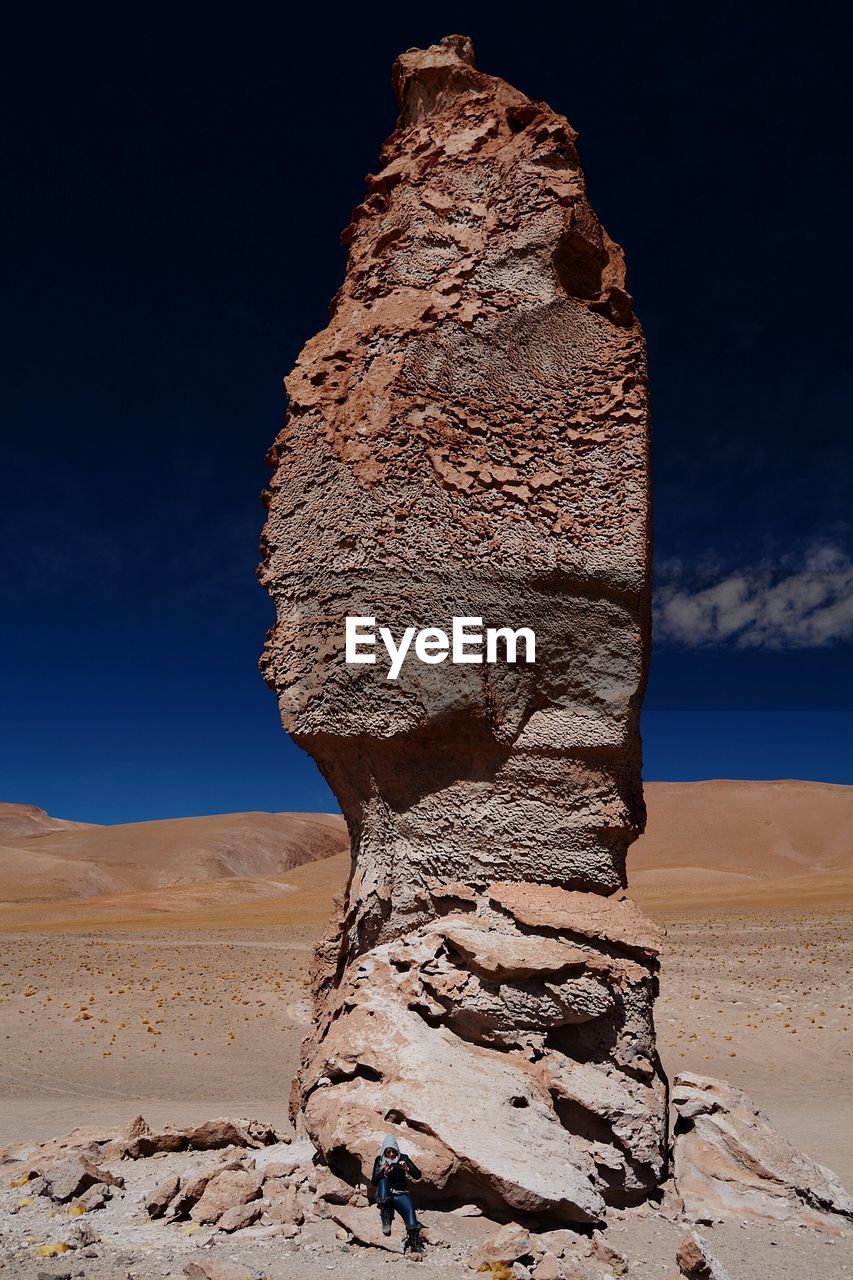 Man sitting by tall stack rock at atacama desert against blue sky