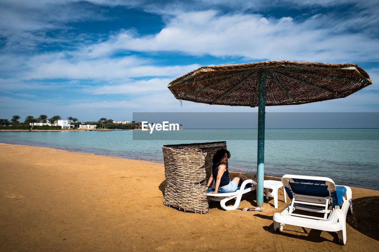 Woman looking away while sitting by parasol at beach