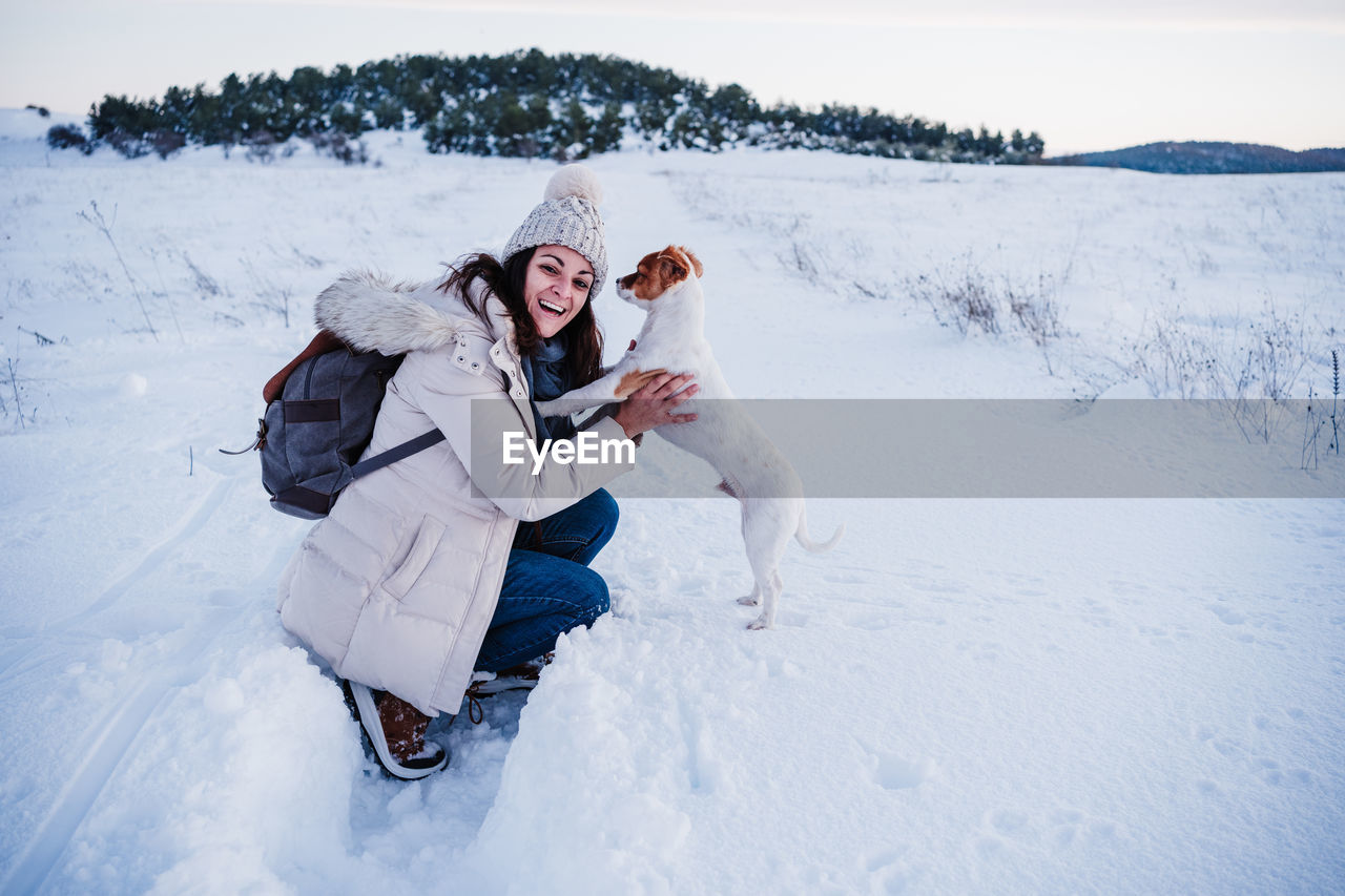 Happy woman in snowy mountain holding cute jack russell dog in arms. winter season. nature at sunset