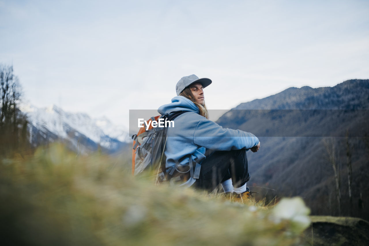 Man with backpack sitting with eyes closed on mountain