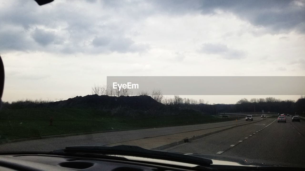 CAR ON ROAD AGAINST CLOUDY SKY SEEN THROUGH WINDSHIELD