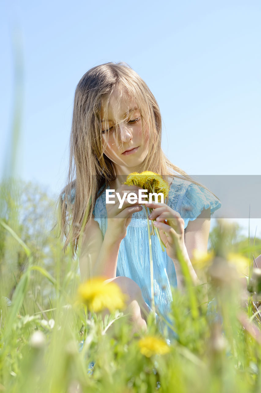 Girl holding yellow flower on field against clear sky