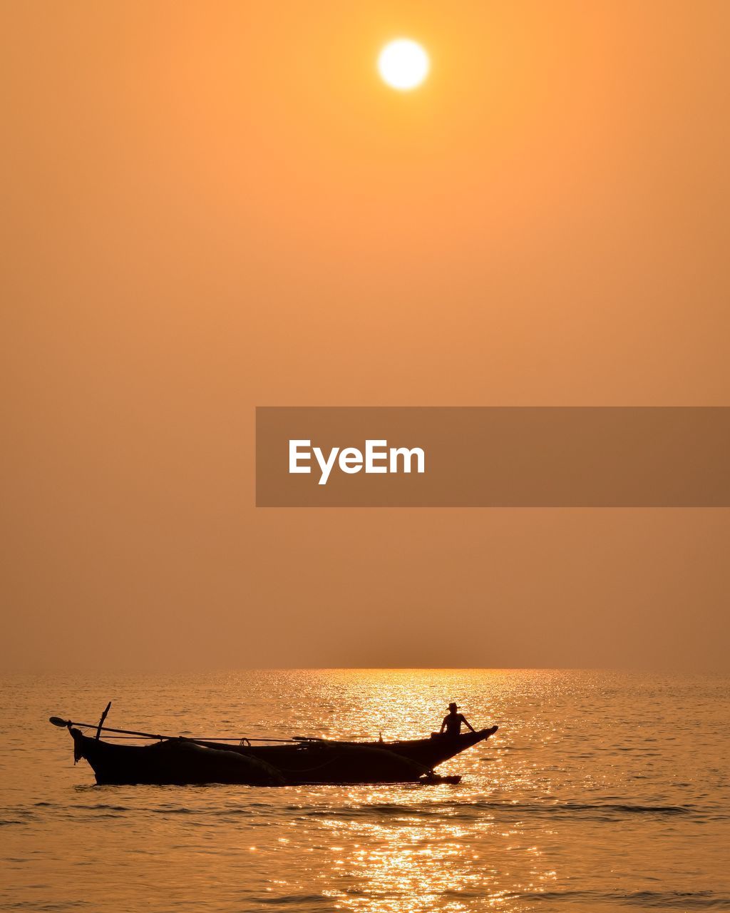 Silhouette man in boat on sea against orange sky
