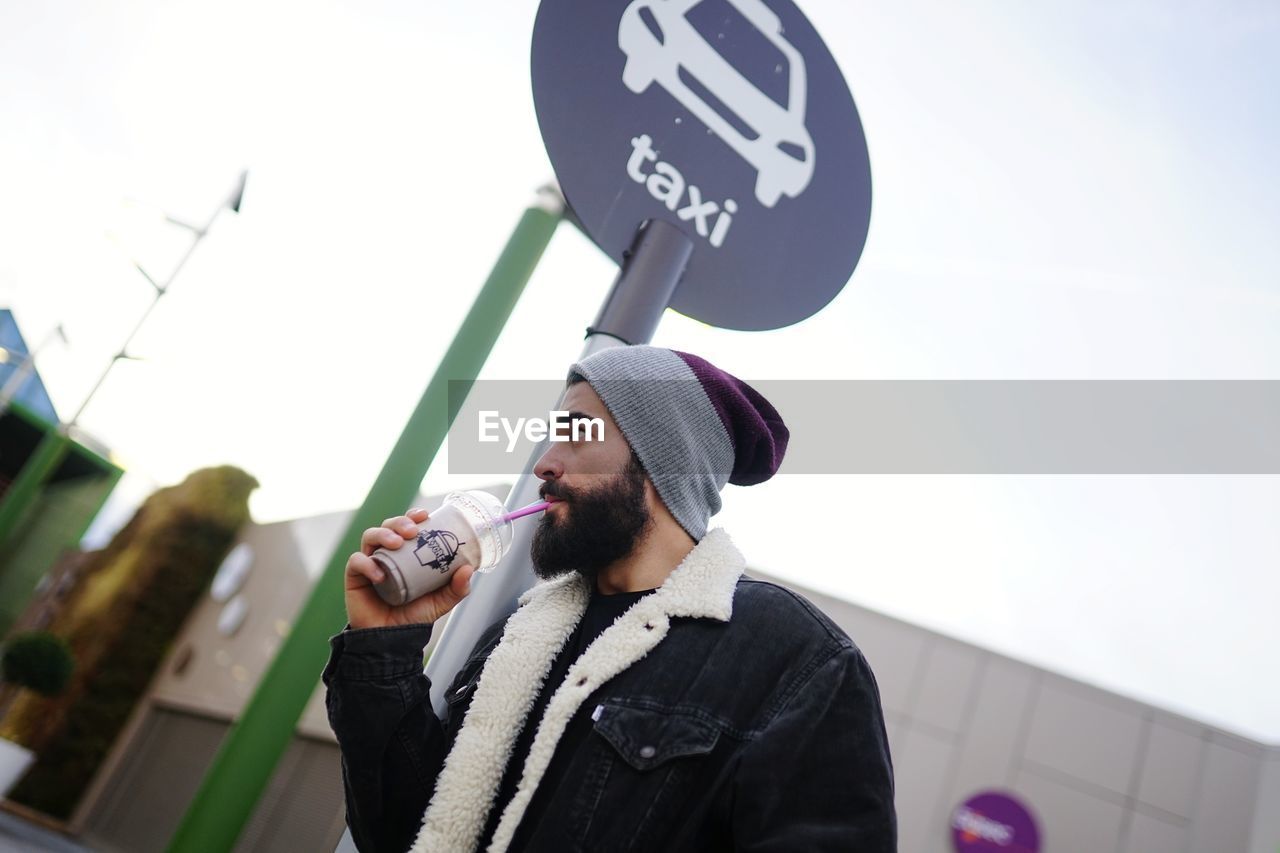 Low angle view of man hanging drink while standing by road sign
