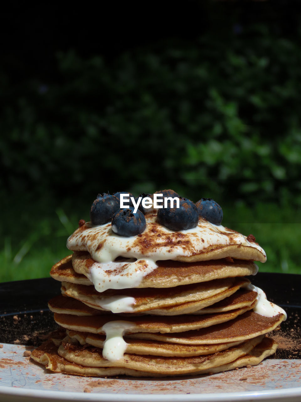 Stack of breakfast pancakes in the sun. topped wi the yoghurt, blueberries and cocoa powder.