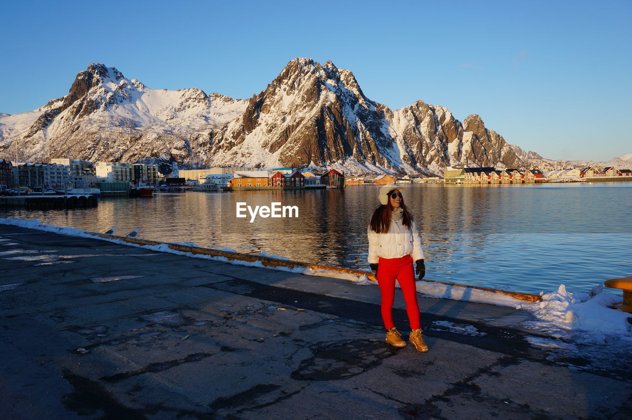Full length of woman standing against snowcapped mountain by lake