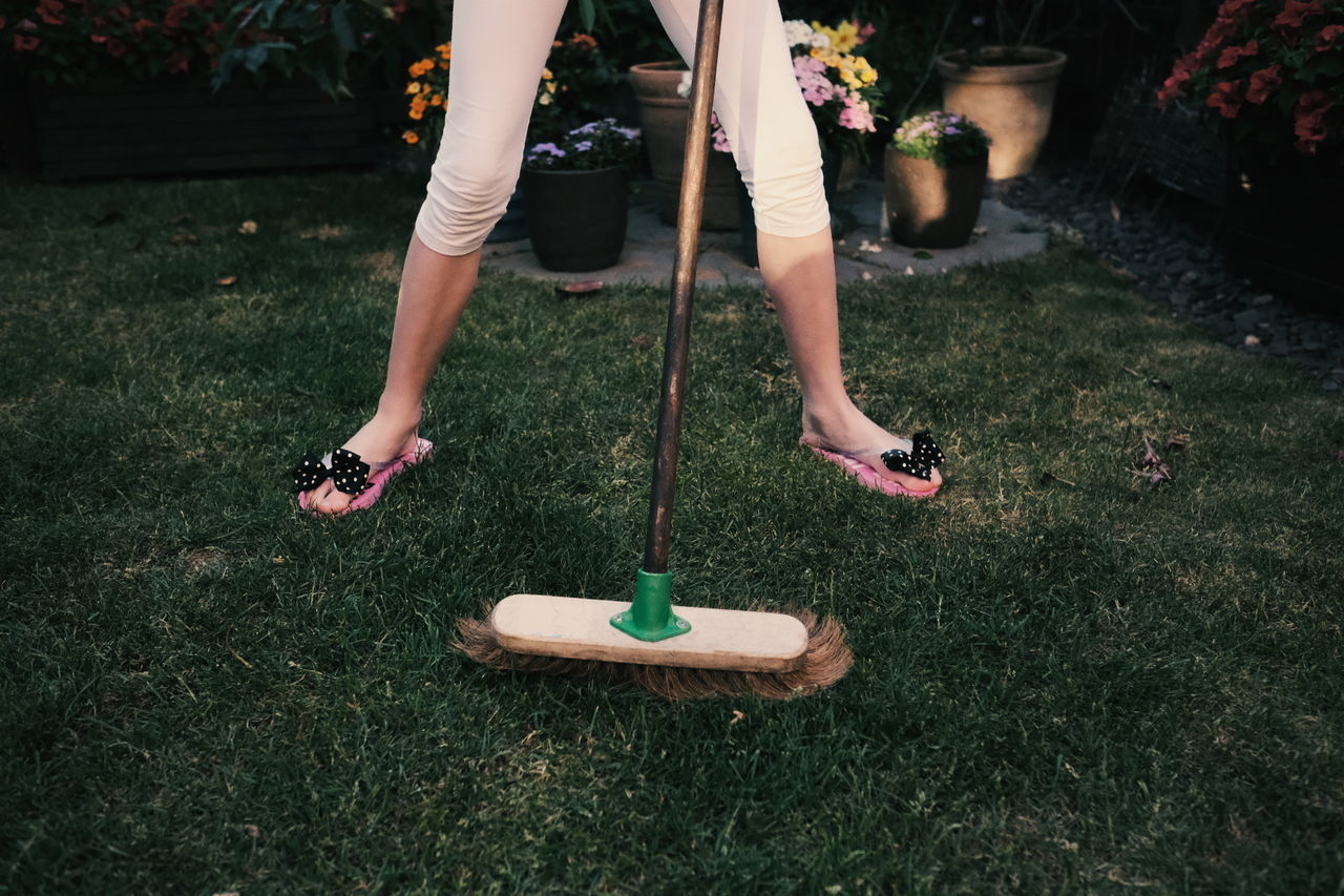 Low section of woman standing with gardening equipment on grass at back yard